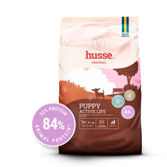 Ração seca Husse Puppy Active Life para cachorros de raças pequenas num saco castanho e rosa com 84% de proteína animal.