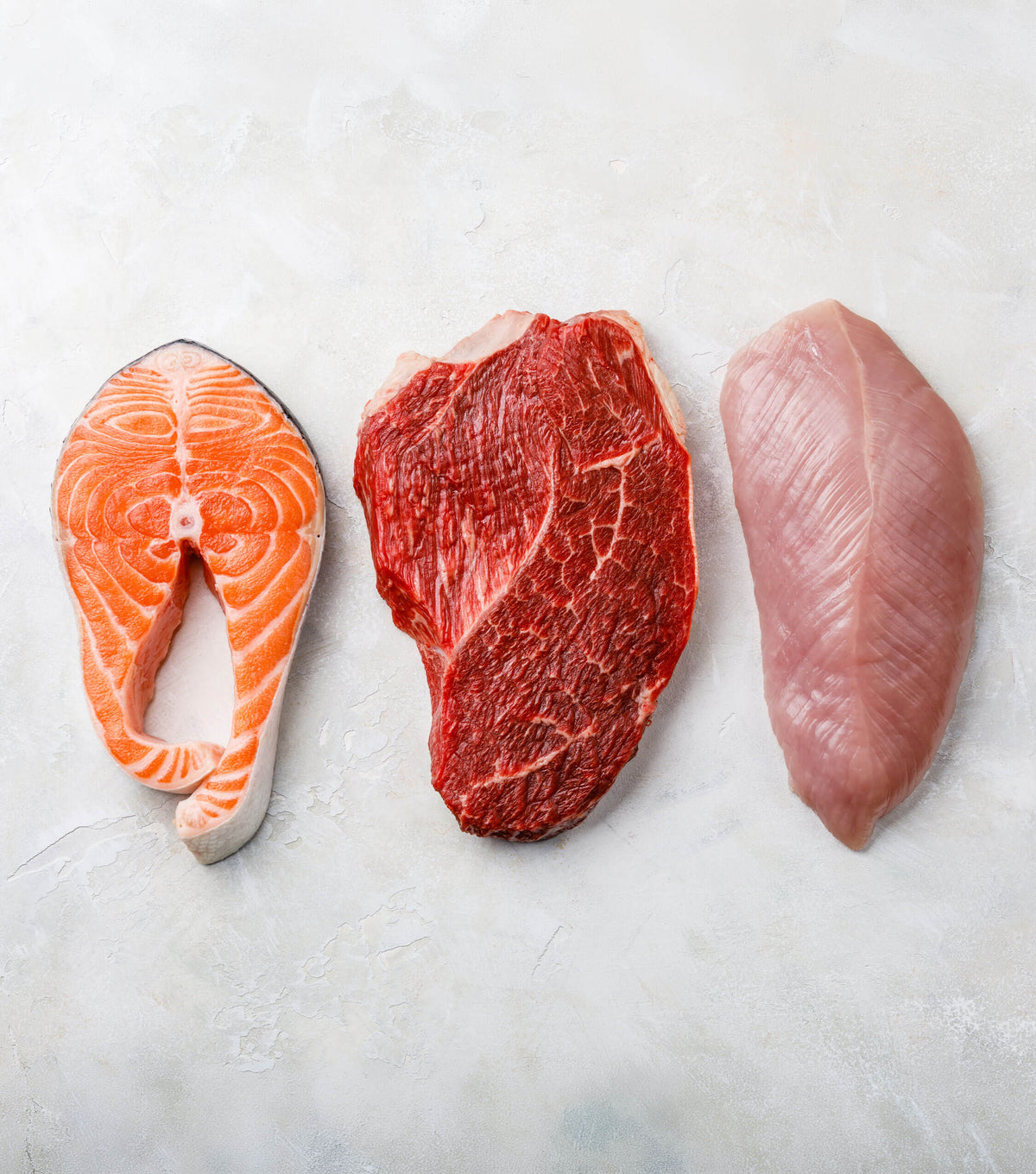 Fresh salmon, beef and chicken fillets laid out on a marble surface
